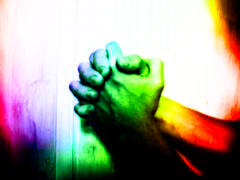 Två händer knäppta i bön, färgade i regnbågsfärgerna