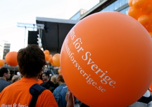 Orange ballong med texten "Allians för Sverige" och en folksamling i bakgrunden.